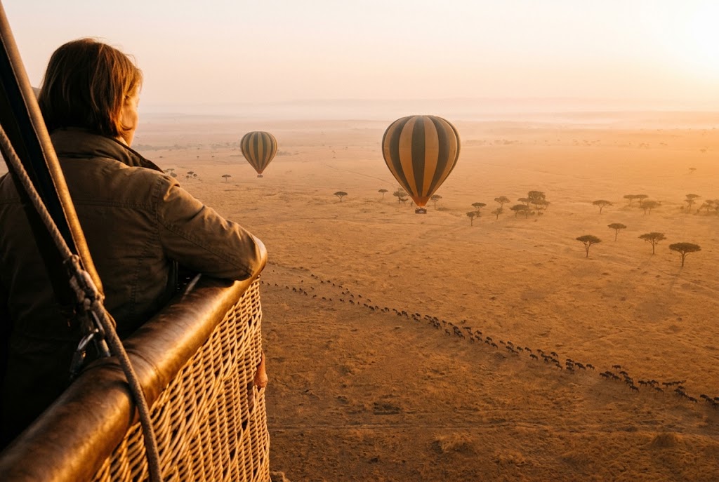 Hot-air balloons floating over the Serengeti plains at sunrise, with wildebeest below, on a Tanzania safari